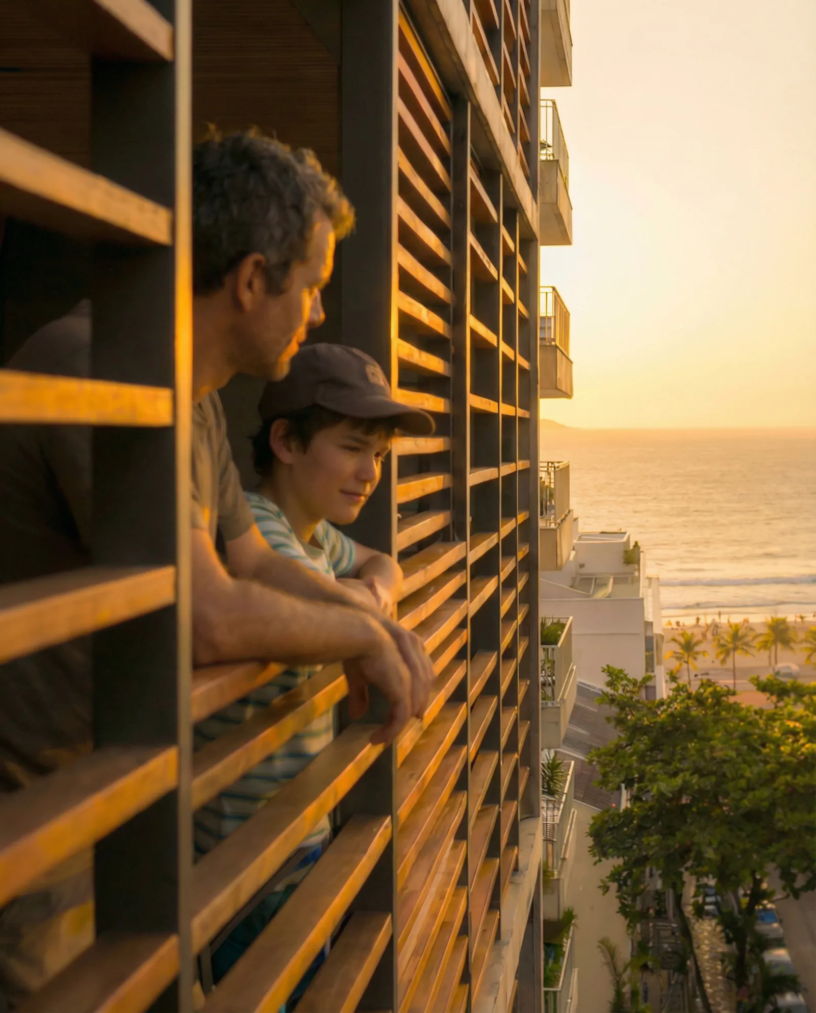 Pai e filho na varanda ao pôr do sol, com o mar ao fundo